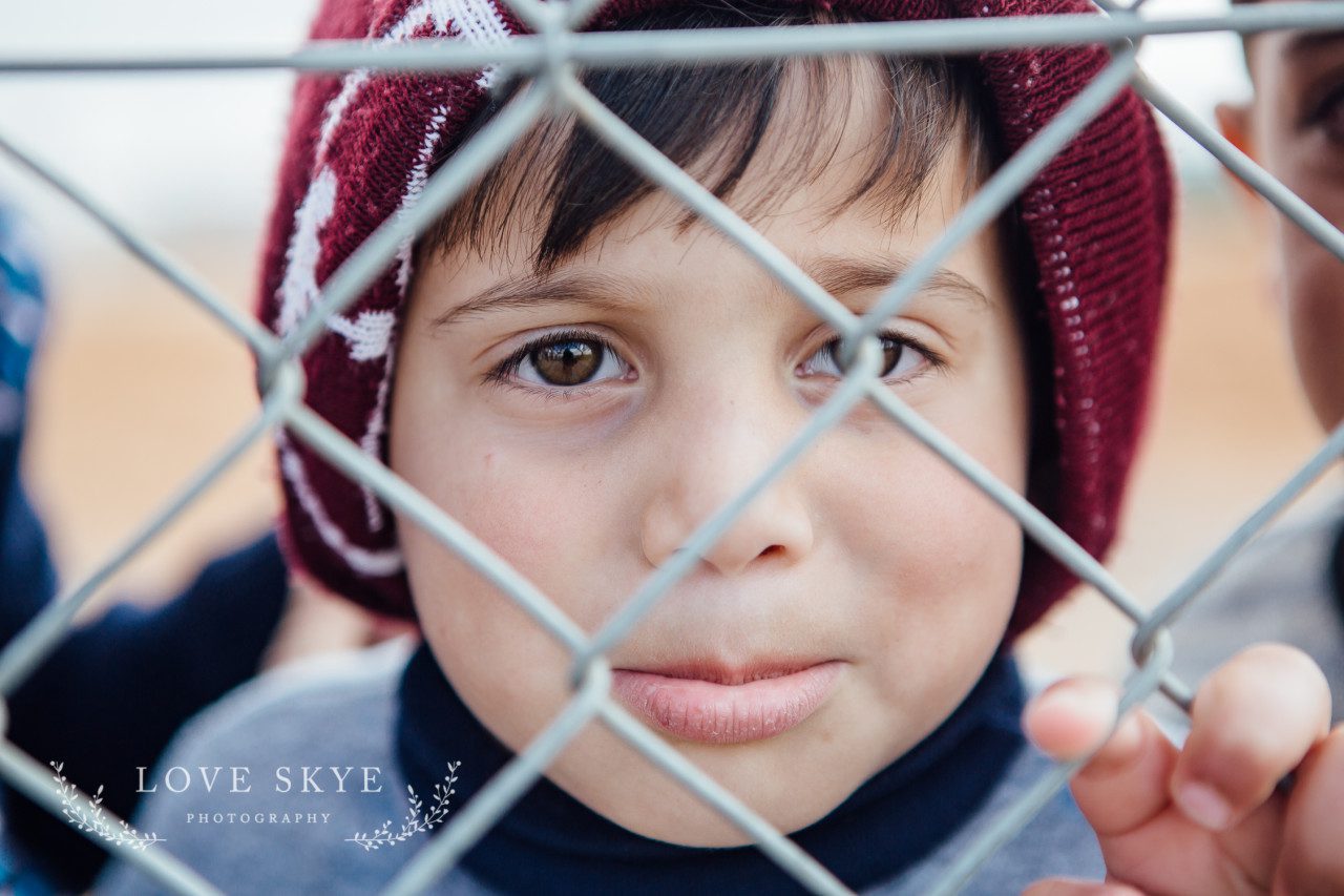 Young Syrian refugee boy holds onto link fence at Azraq refugee camp Jordan