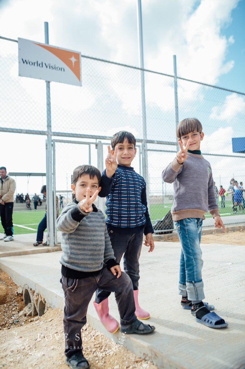 Young boys make symbol of peace outside World Vision football pitch Azraq refugee camp Jordan 