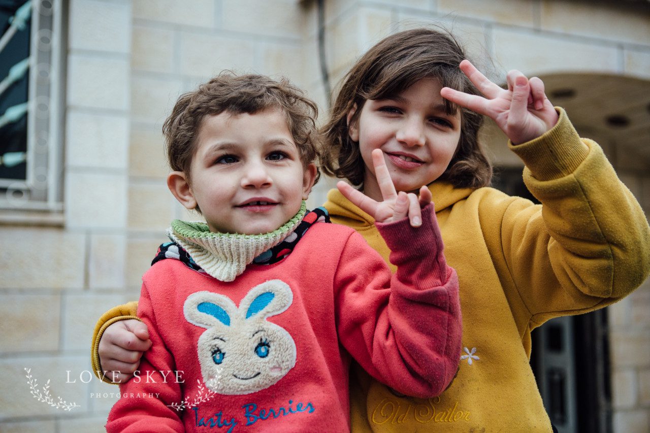 Barefoot Syrian refugee children Jordan give peace symbol to photographer