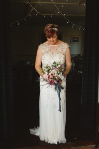 Beaming bride in wedding dress short pink hair looking down holding bouquet