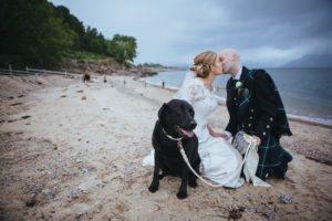 Bride and groom kiss on beach their dog looks to camera