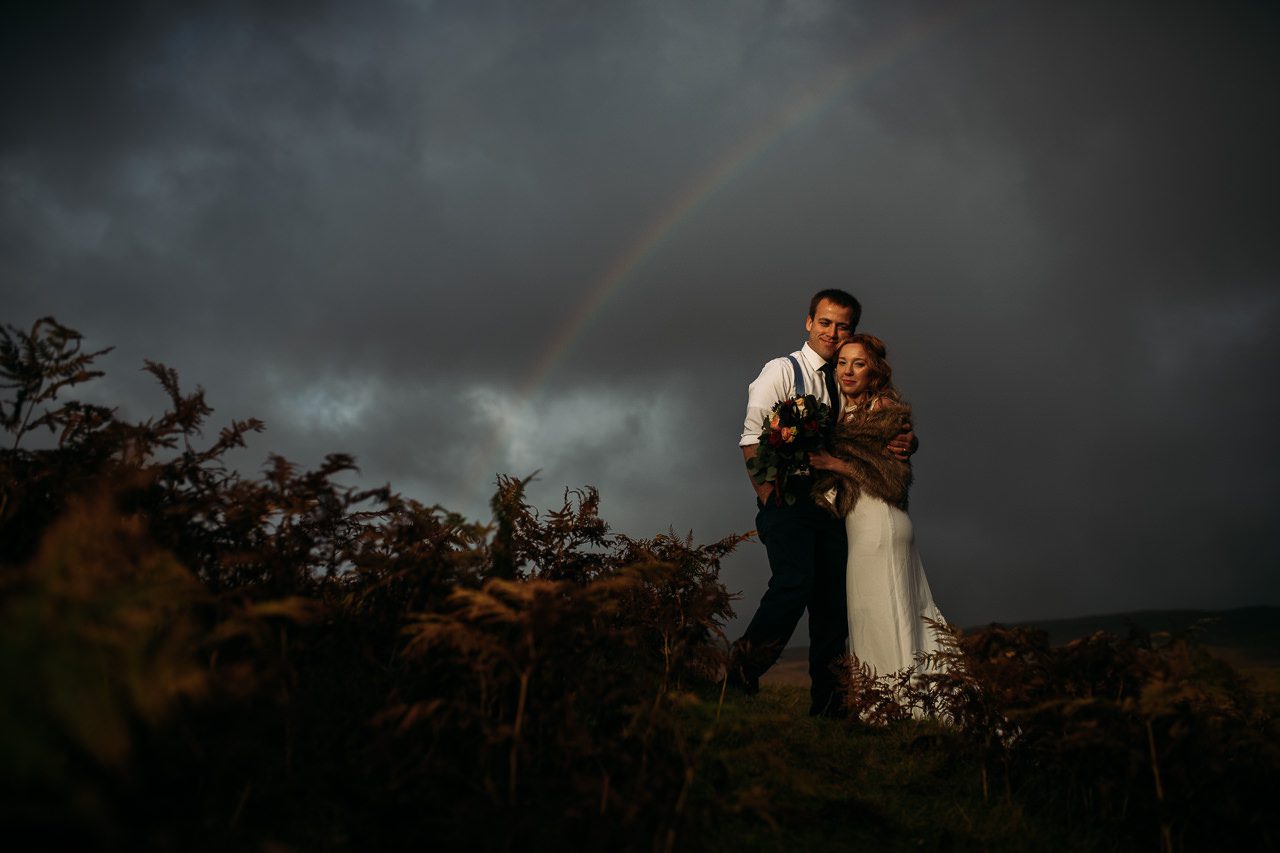 Bride and Groom embrace late afternoon light and rainbow Isle of Skye