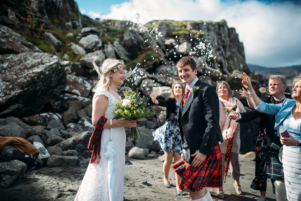 Confetti scatters over bride and kilted groom Staffin beach Isle of Skye