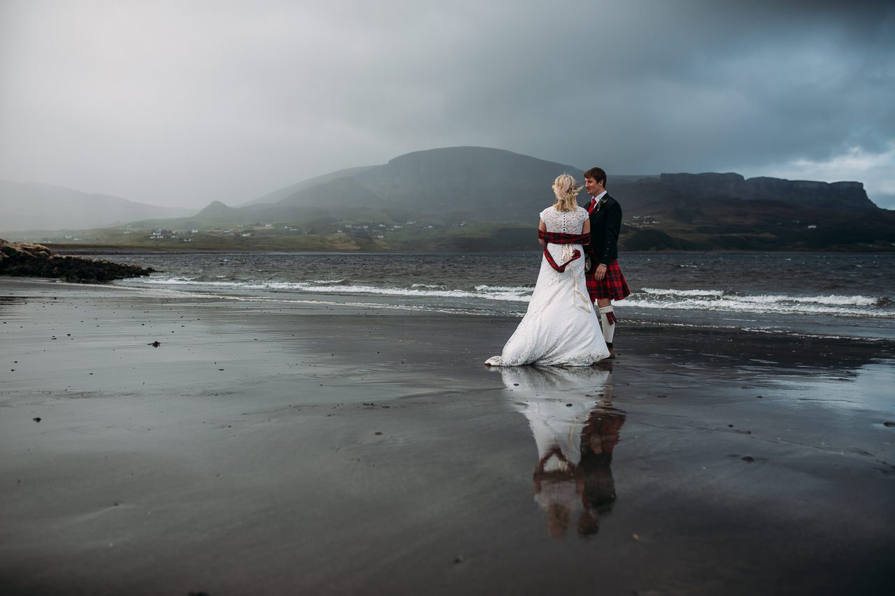 Wedding couple reflected in wet sands Staffin beach Isle of Skye Quiriaing in bakground