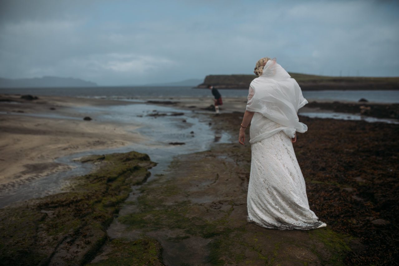 Bride in rain cape looking for dinosaur footprints Staffin beach Isle of Skye
