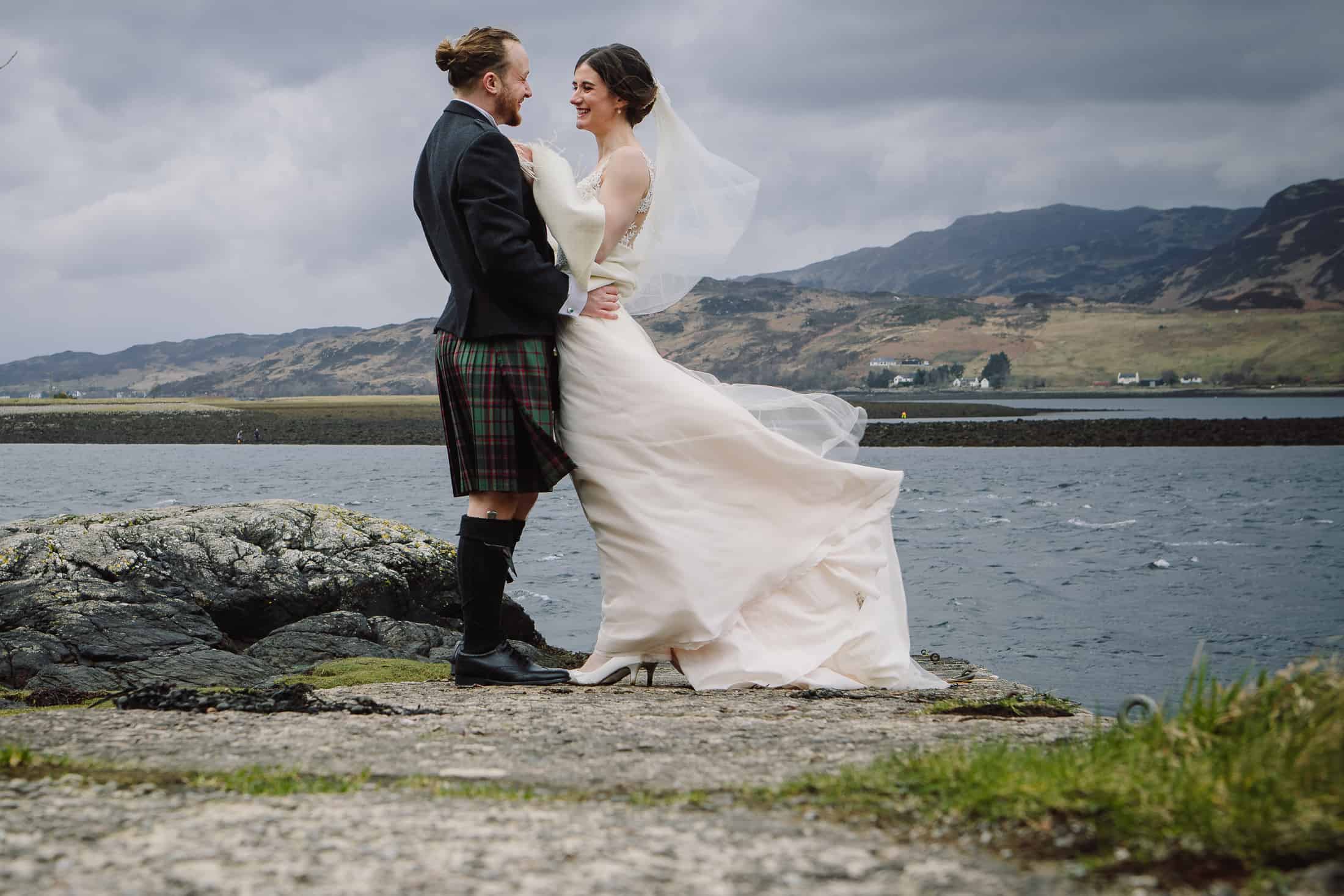 Bride and groom on slipway wind ruffling dress Eilean Donan Castle