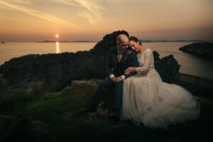 wedding couple sit at Duntulm Castle Isle of Skye at sunset