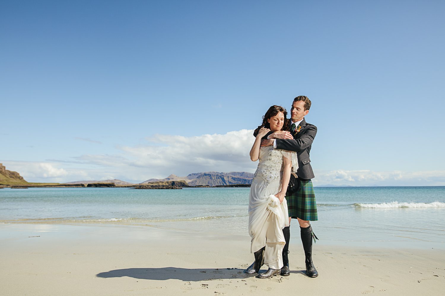 Bride in dress and wellies and kilted groom on white sand beach Isle of Canna
