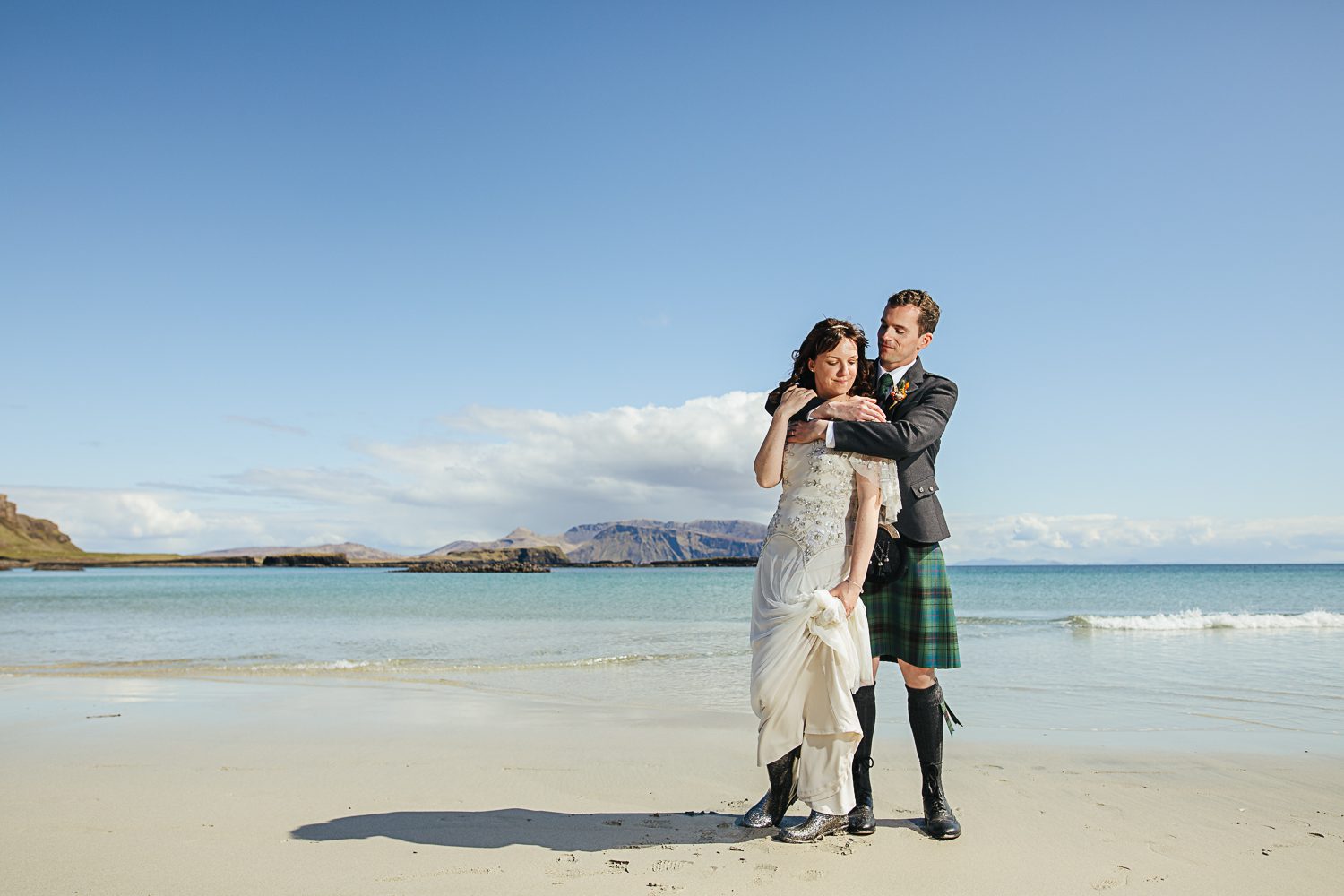 Bride in dress and wellies and kilted groom on white sand beach Isle of Canna