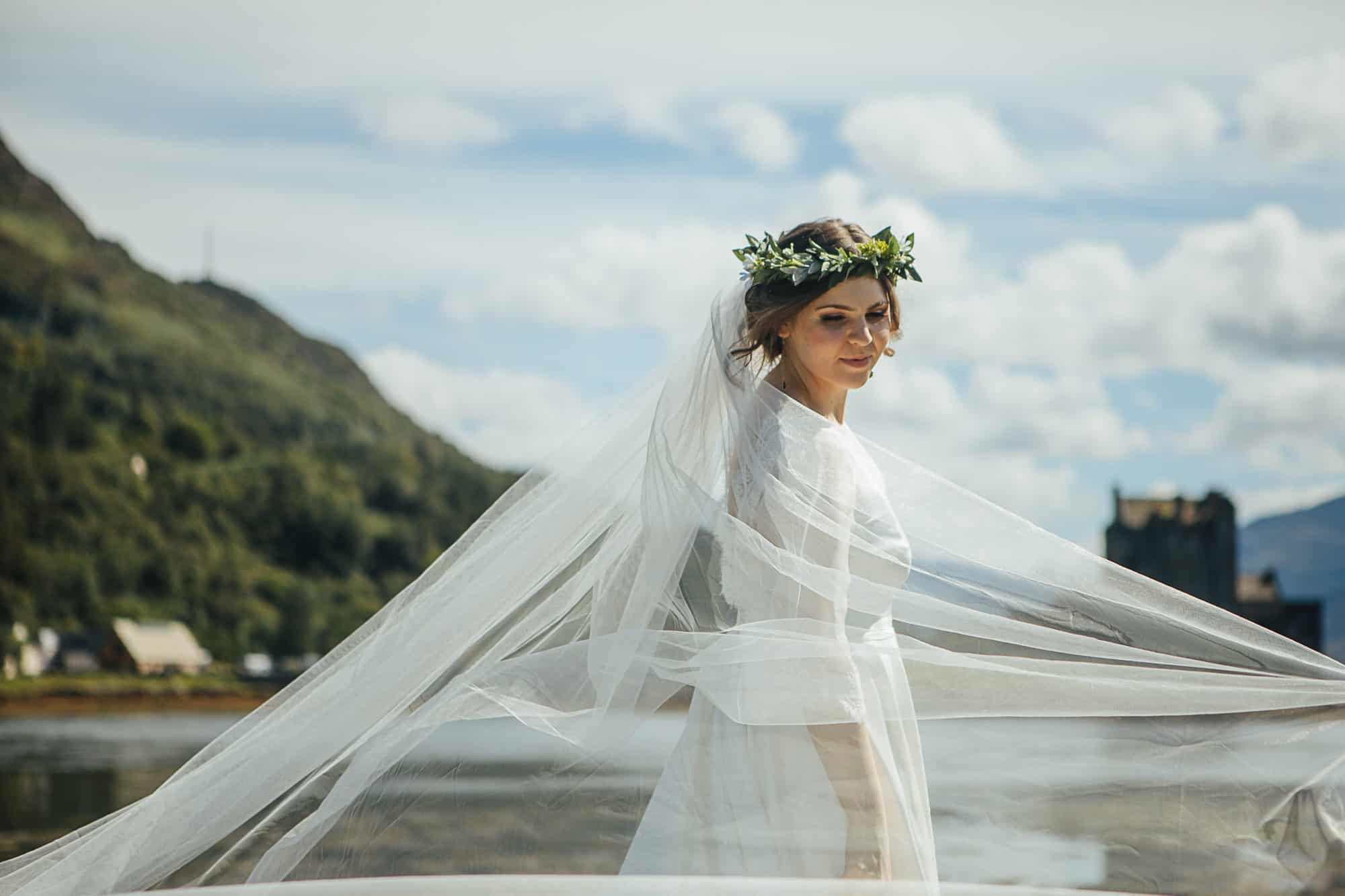 Bride with flower crown and billowing veil outside Eilean Donan Castle