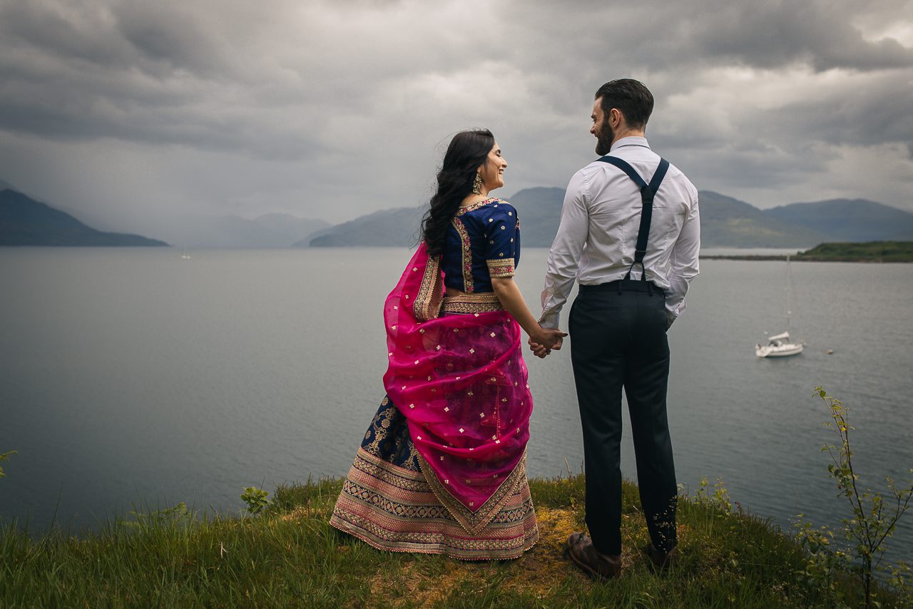 Elopement couple overlooking the sea on Isle of Skye. Bride wears sari, groom wears braces
